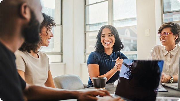 Four people sitting at a desk in a meeting room smiling.