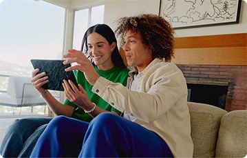 Two people sitting on a couch in a modern living room, looking at a tablet device together.