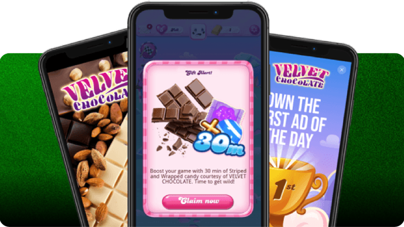 Three smartphones displayed against a green striped background: the center phone shows a candy-themed game screen with a reward message offering 30 minutes of boosters, while the left and right phones feature Velvet Chocolate ads.